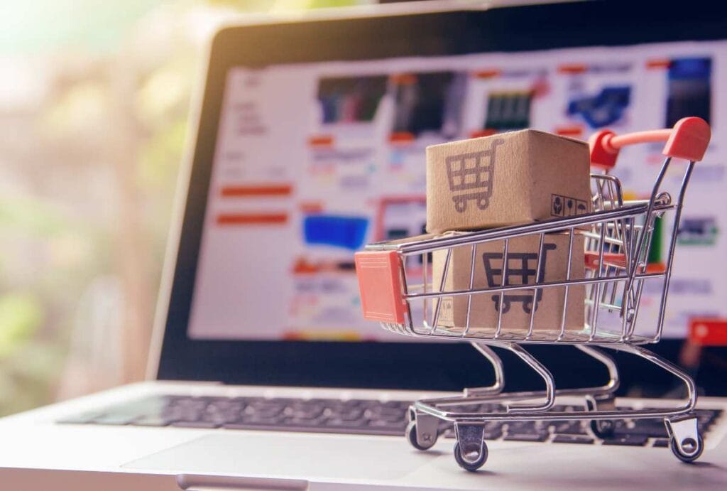 Image of a miniature shopping cart with boxes sitting on a laptop to discuss that amazon is a product distributor