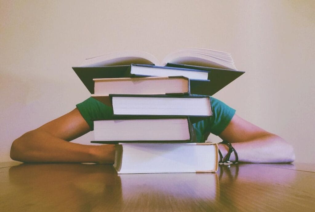 A photo of a person with their head down on a table behind a stack of books illustrates the complexities of baby carrier regulations.