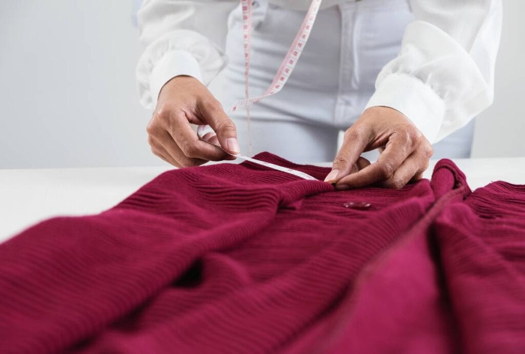 A closeup of someone in a white shirt with hands measuring fabric is meant to imply they are testing for the EU baby sling standard
