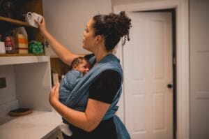 Babywearing normal breathing Adult puts an object on a shelf while baby sleeps in a blue wrap.